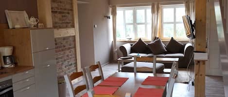 A cozy living area with a sofa, a dining table with chairs, a kitchen with a refrigerator, and a brick wall.