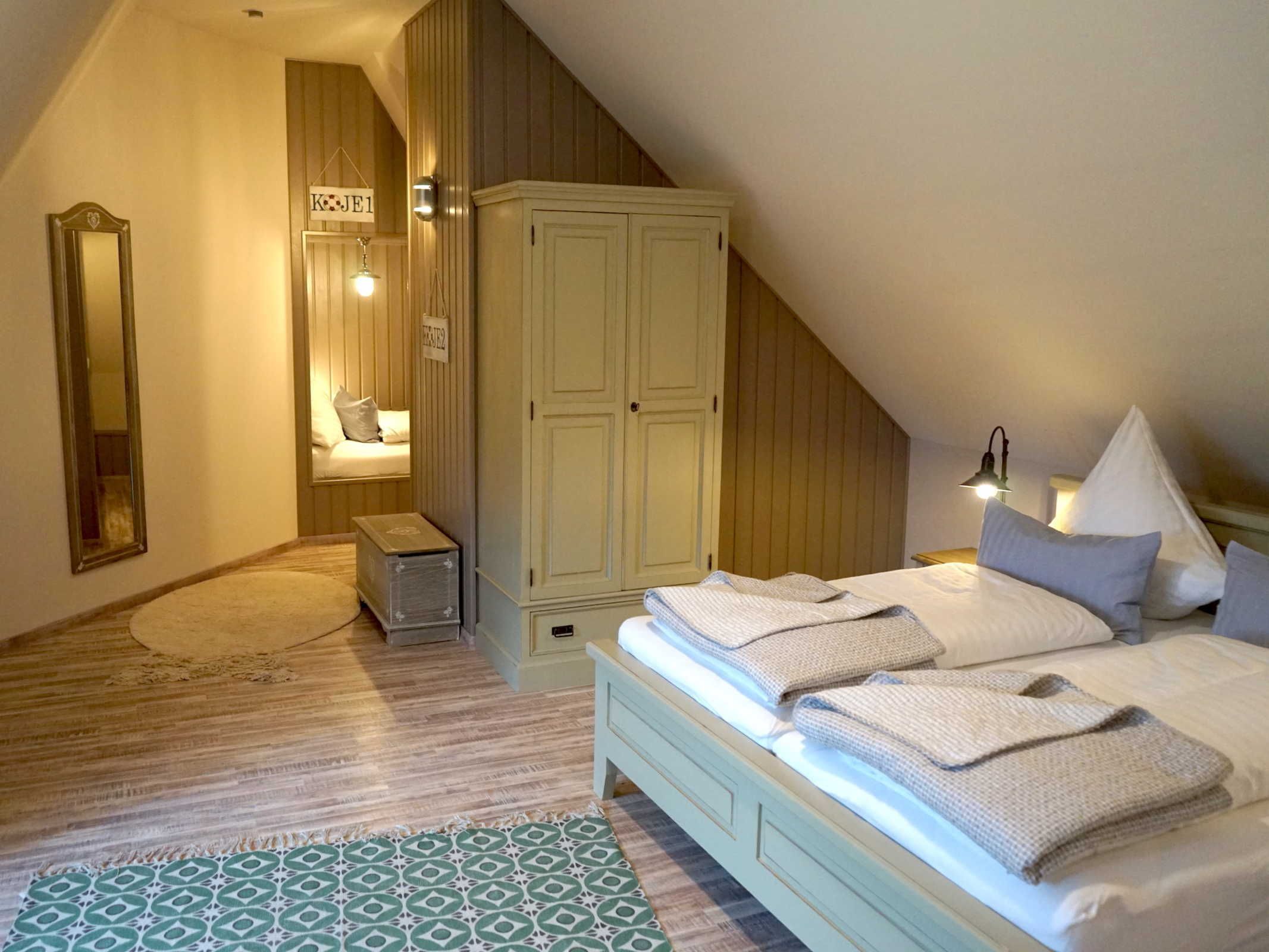 Een slaapkamer met een schuine kap, een bed met kussens en dekbed, een kledingkast, een spiegel en een bedlamp.