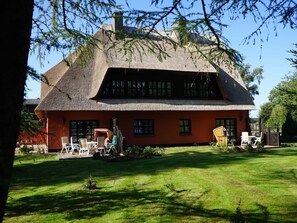 A traditional thatched-roof house with a red facade, a well-maintained lawn, and outdoor seating.