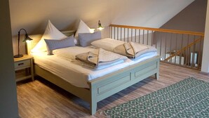 Un dormitorio con cama, almohadas, mesita de noche, lámpara y alfombra estampada.
