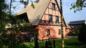 A traditional half-timbered house with a steeply pitched roof, surrounded by a well-maintained garden and trees.
