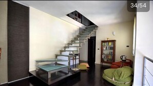 Un salon moderne avec un escalier en verre, un fauteuil en forme de haricot vert et une bibliothèque.