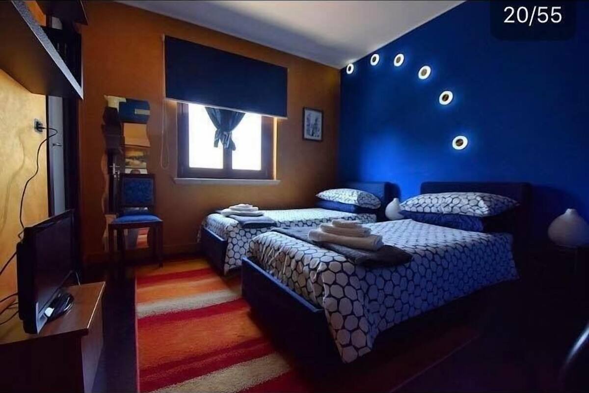 Une chambre à coucher avec un lit, un bureau avec un ordinateur, une fenêtre avec des rideaux et un mur orné de luminaires circulaires.