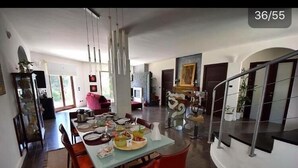 Un vaste espace dédié à la salle à manger, avec une longue table dressée pour le repas, entourée de chaises modernes et agrémentée d’un luminaire contemporain.