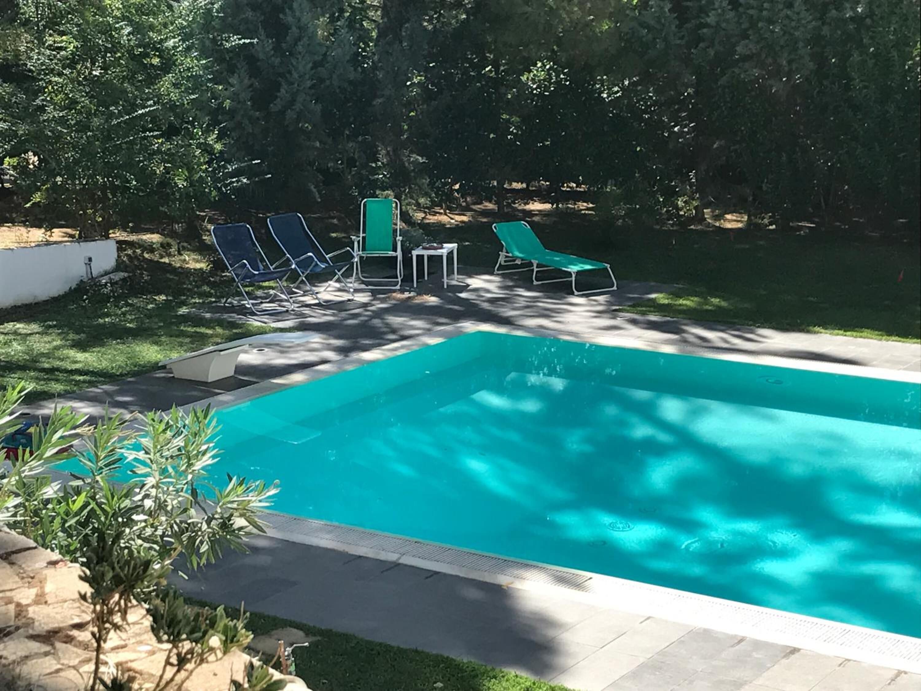 A rectangular swimming pool with a tiled edge, surrounded by a stone patio. There are four lounge chairs and a small table near the pool.