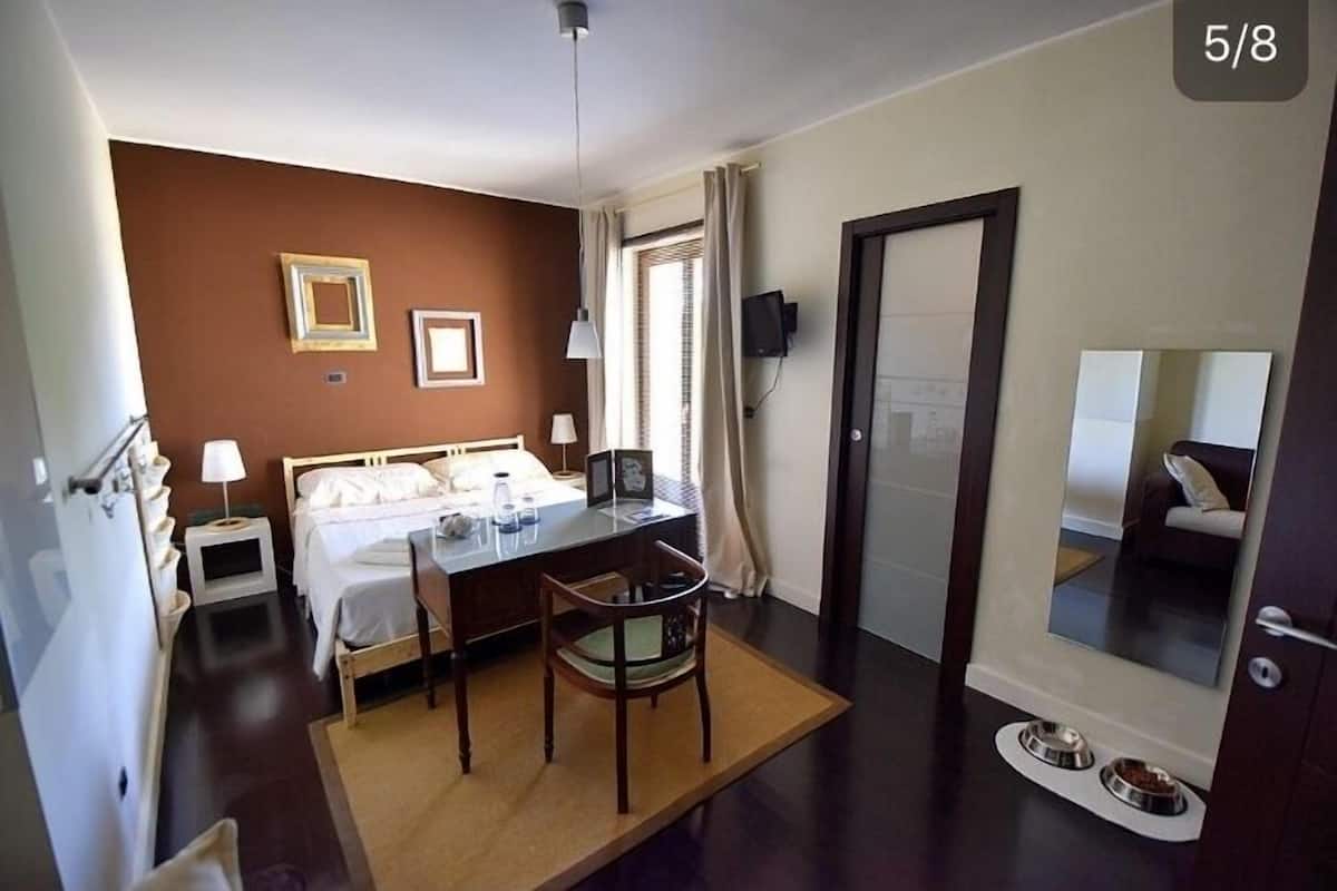 Une chambre d’hôtel comprenant un lit, un bureau, une chaise, une table de chevet, une lampe et un grand miroir.