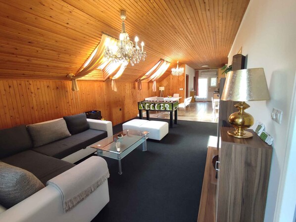 A cozy room with a wooden ceiling, a sofa, a coffee table, a lamp, and a billiards table.