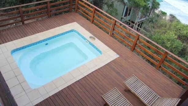 Une terrasse en bois avec un jacuzzi, des rampes en bois et une vue sur l’océan.