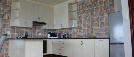 Una cocina con armarios blancos, microondas, refrigerador de acero inoxidable y salpicadero de azulejos.