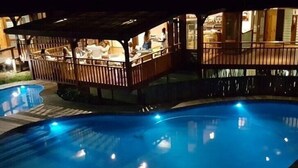 Una piscina con cubierta de madera y zona techada con mesas y sillas.