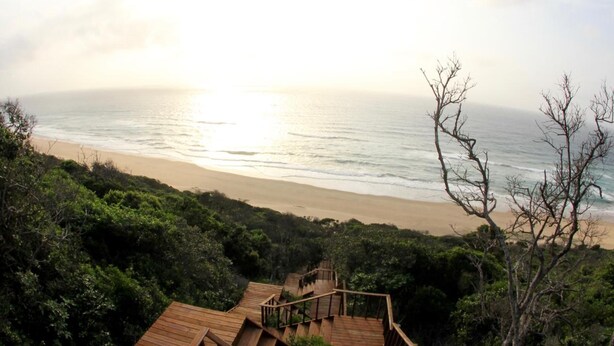 Una terraza de madera con una escalera que baja a la playa.