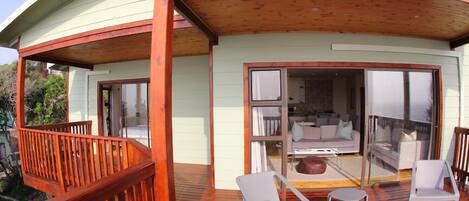 Un edificio curvo con terraza de madera, asientos al aire libre y puerta de vidrio que da a un espacio interior.