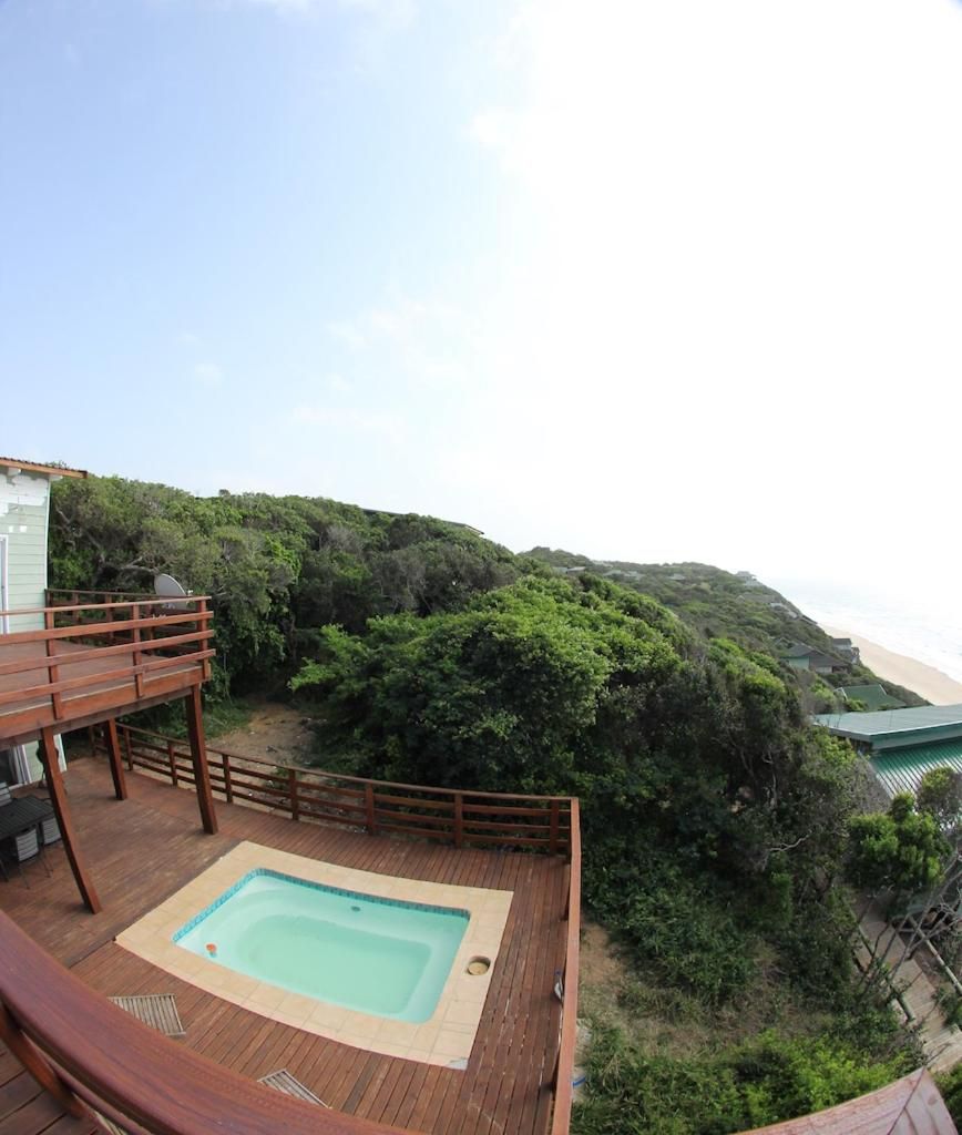 Una terraza de madera con un jacuzzi, con vistas a una playa y abundante vegetación.