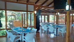 Amplio espacio interior con vigas de madera y ventanas grandes, con varias mesas y sillas dispuestas para comer.