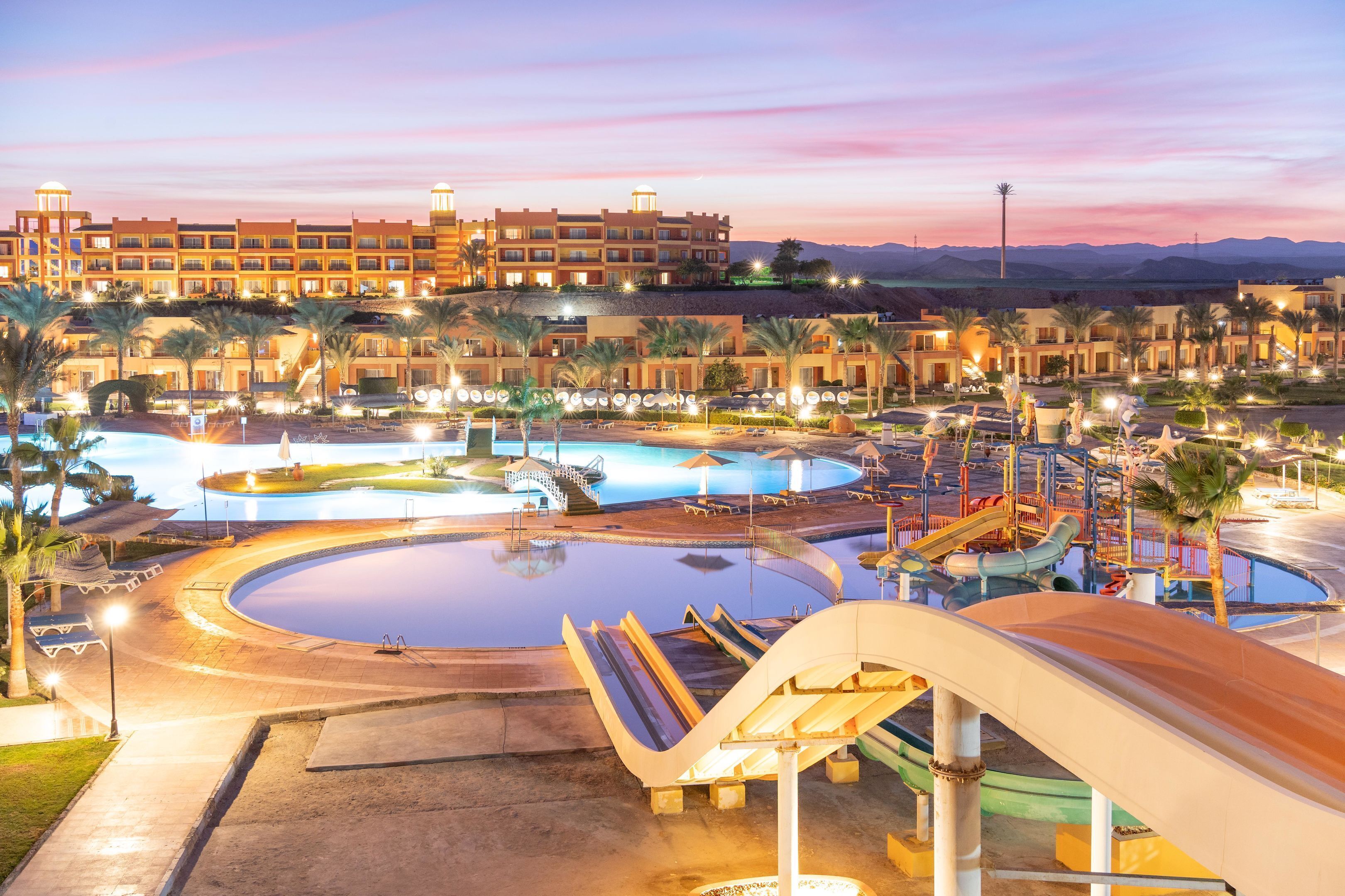 A resort with multiple swimming pools, a water slide, and a large building with multiple balconies.