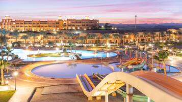 A resort with multiple swimming pools, a water slide, and a large building with multiple balconies.