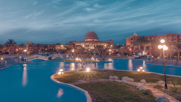 Un área de piscina en un resort, con una piscina central grande, piscinas secundarias más pequeñas y un puente que las conecta.