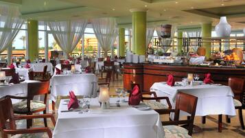 A restaurant with multiple tables set for dining, featuring white tablecloths and red napkins.