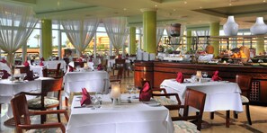 A restaurant with multiple tables set for dining, featuring white tablecloths and red napkins. - Malikia Resort Abu Dabbab (Marsa Alam)