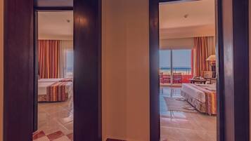 A hotel room with a large bed, a balcony with a view of the beach, and a separate sitting area with a table and chairs.