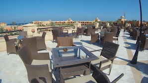 Una terraza en la azotea con mobiliario de mimbre y una vista despejada del mar y edificios de hotel.