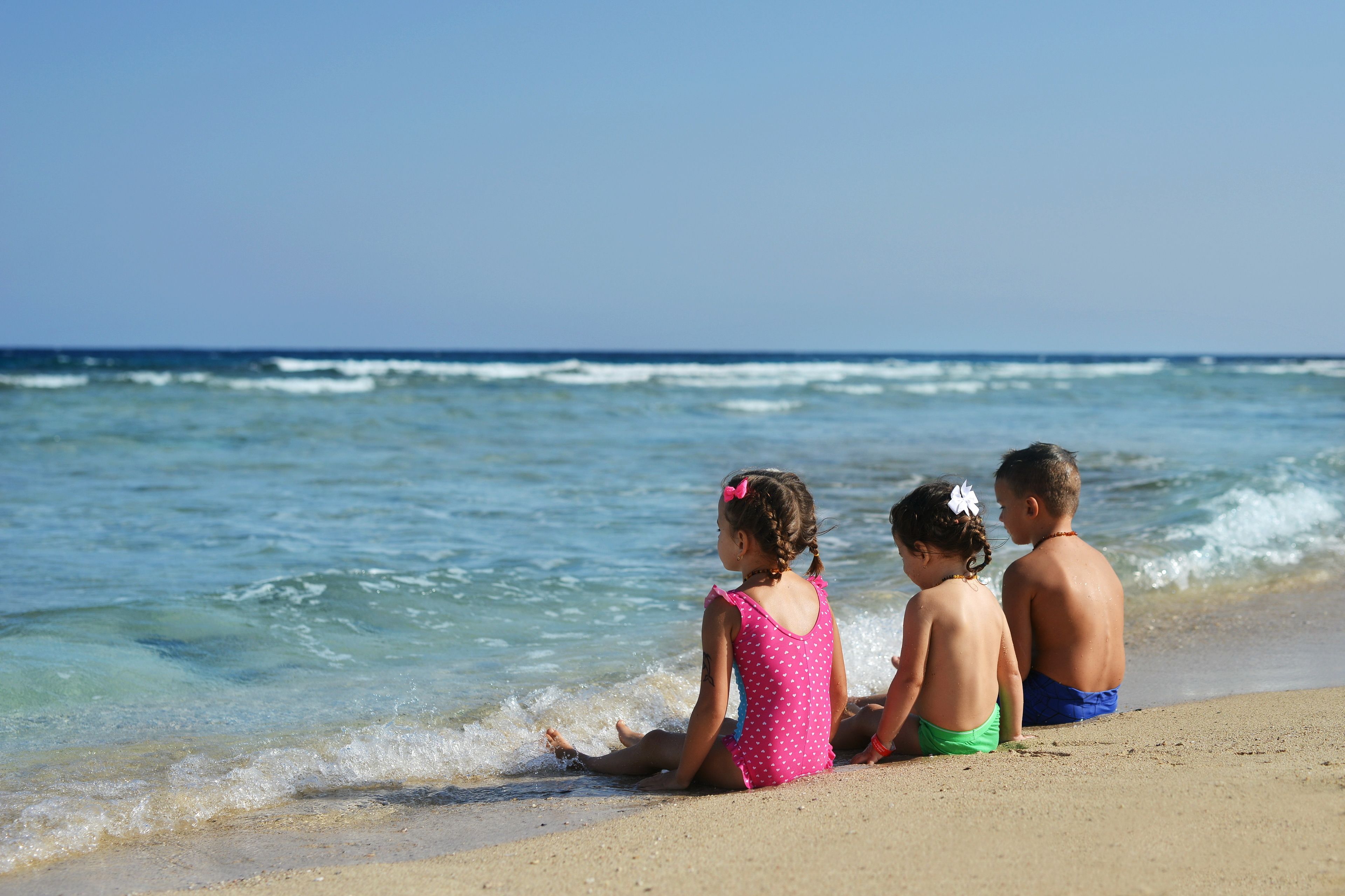 Tres niños sentados en una playa arenosa junto al océano.