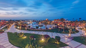 Un resort con zona de piscina, palmeras y senderos bien iluminados.