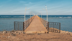 Un muelle de madera que se extiende hacia el mar, con barandillas de metal a ambos lados.