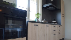 Una cocina moderna con horno empotrado, armarios de madera, un ventanal y una planta en maceta.
