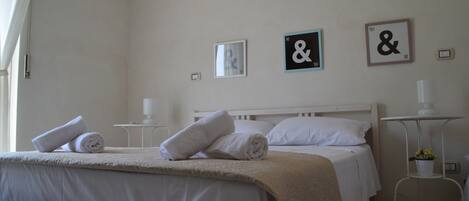 A neatly made bed with rolled towels, a bedside table with a lamp, and two wall-mounted pictures with text.