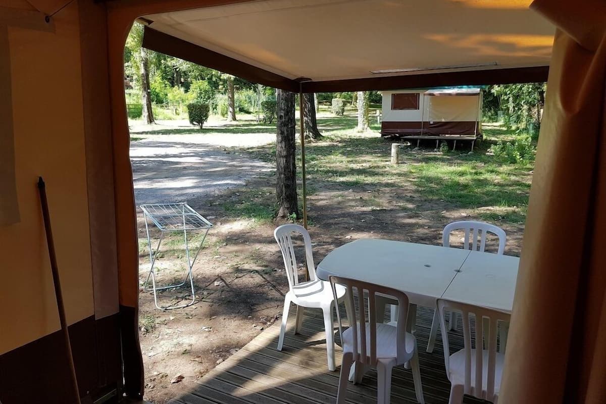 Un espacio al aire libre techado con una mesa, sillas, una parrilla y una tienda de campaña al fondo.