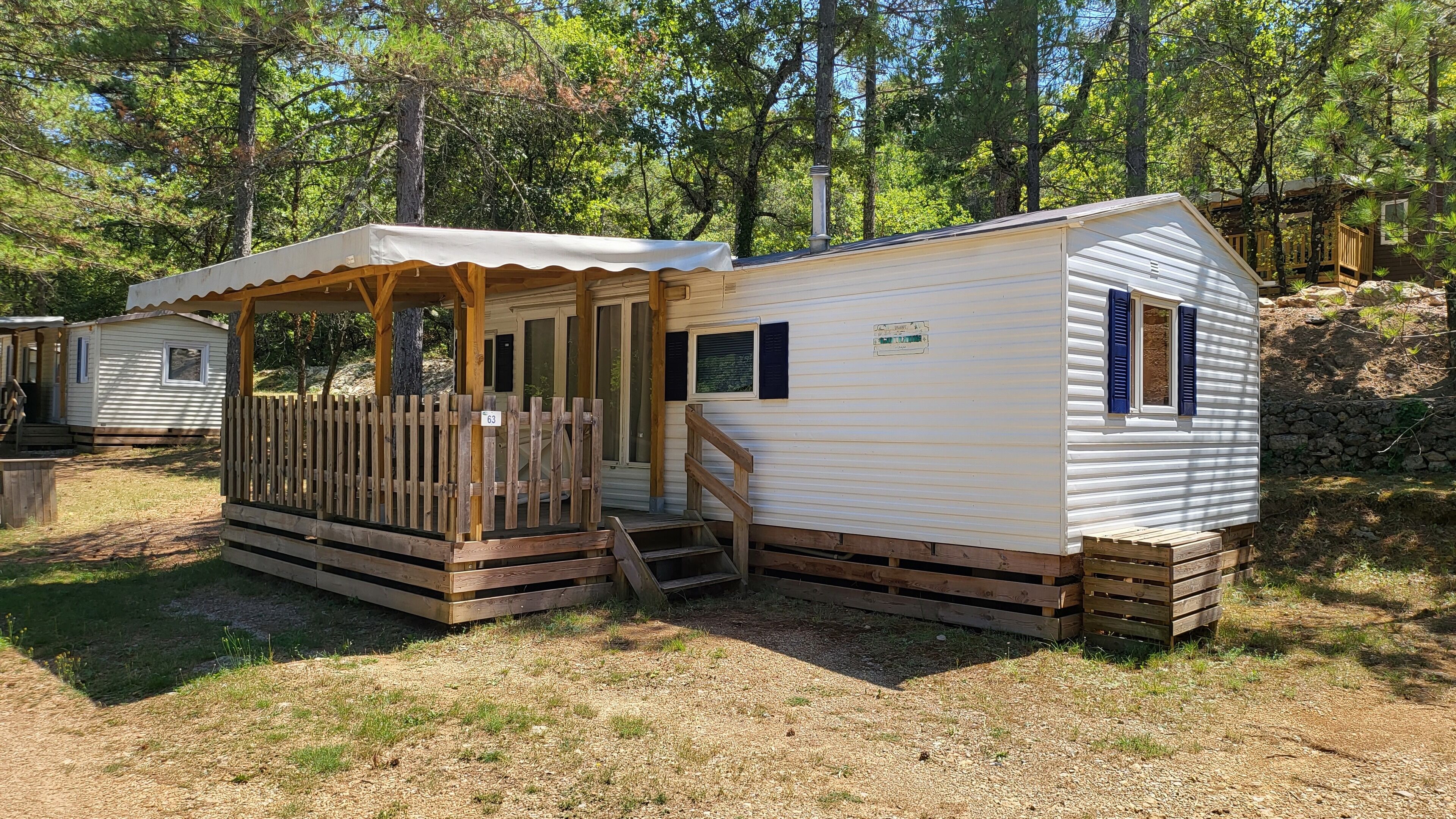 A mobile home with a porch and a small deck, surrounded by trees.
