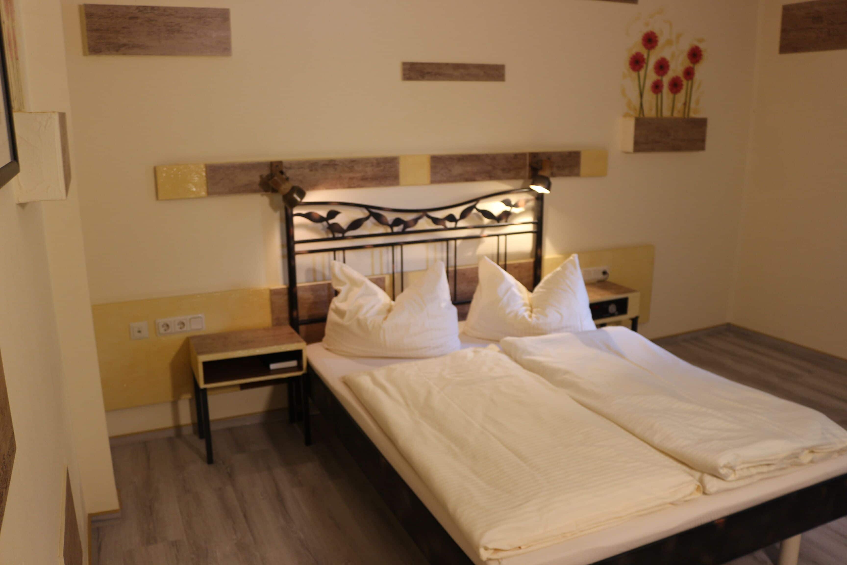 Un letto rifatto con lenzuola bianche, una testiera in legno e un comodino con una lampada.