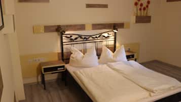 Un letto rifatto con lenzuola bianche, una testiera in legno e un comodino con una lampada.
