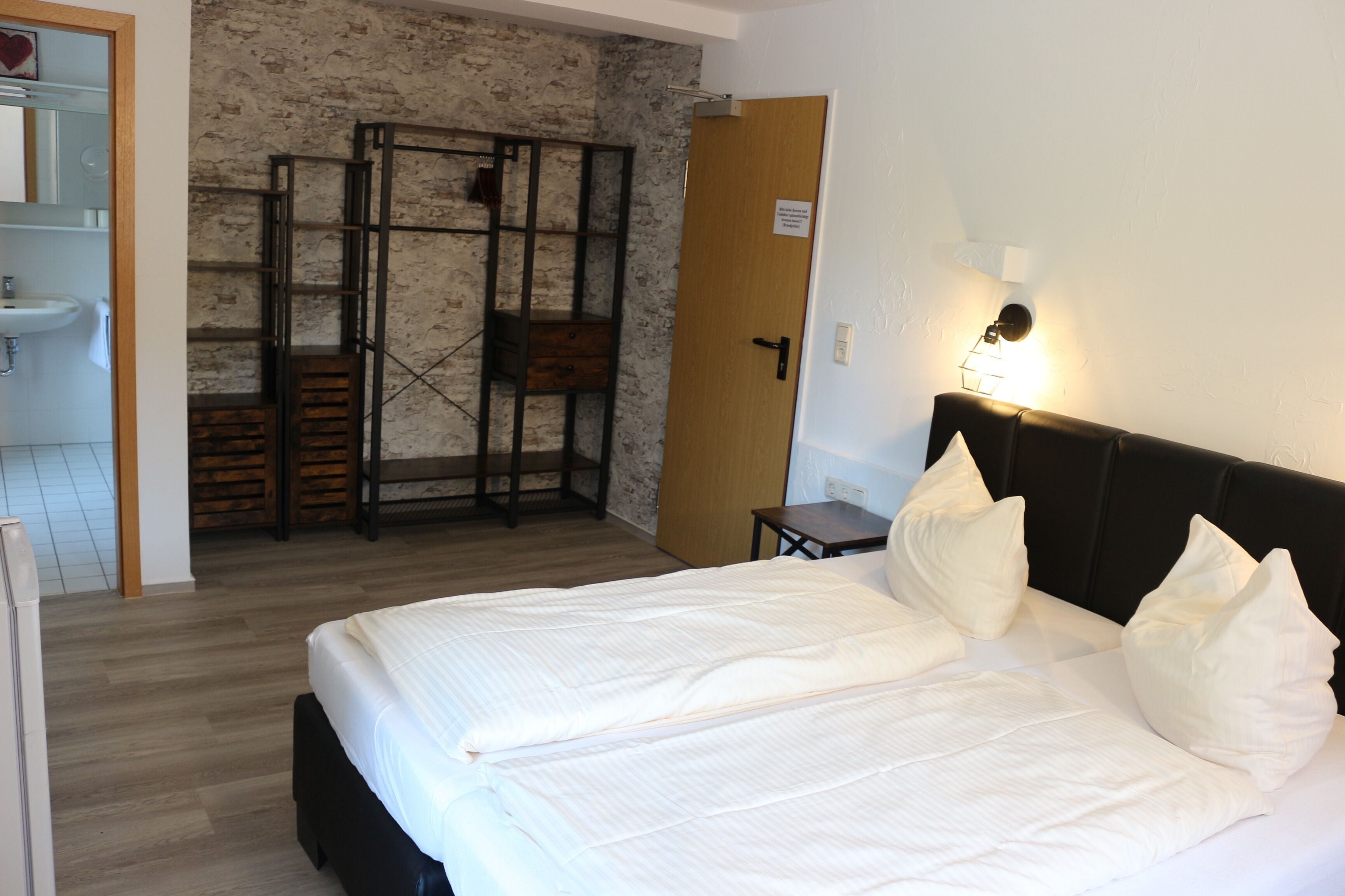 Ein Schlafzimmer mit einem Bett, Nachttischen, einem Wandregal und einer Tür.