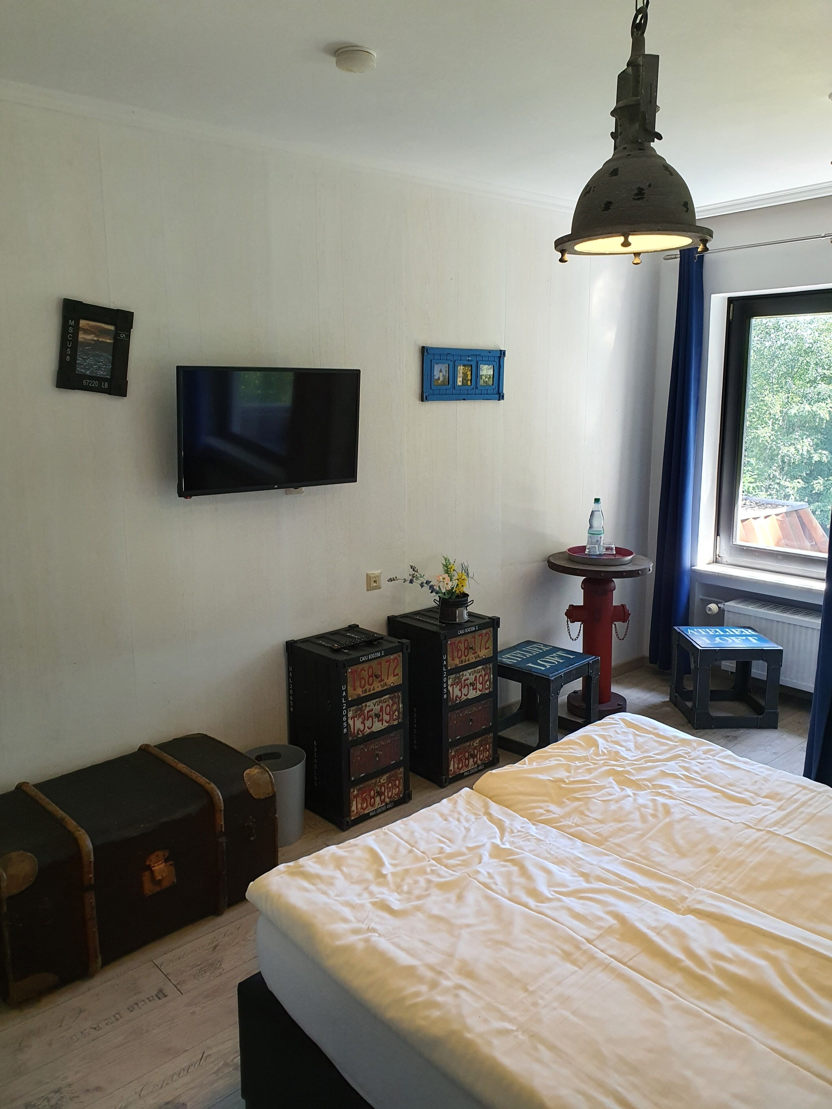 A room with a bed, a television, a small table with a vase, and suitcases against the wall.