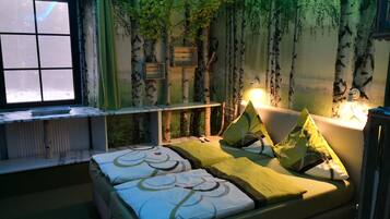 Ein Schlafzimmer mit Bett, Fenster, einer Wand mit Baum-Wandbild und Nachttisch.