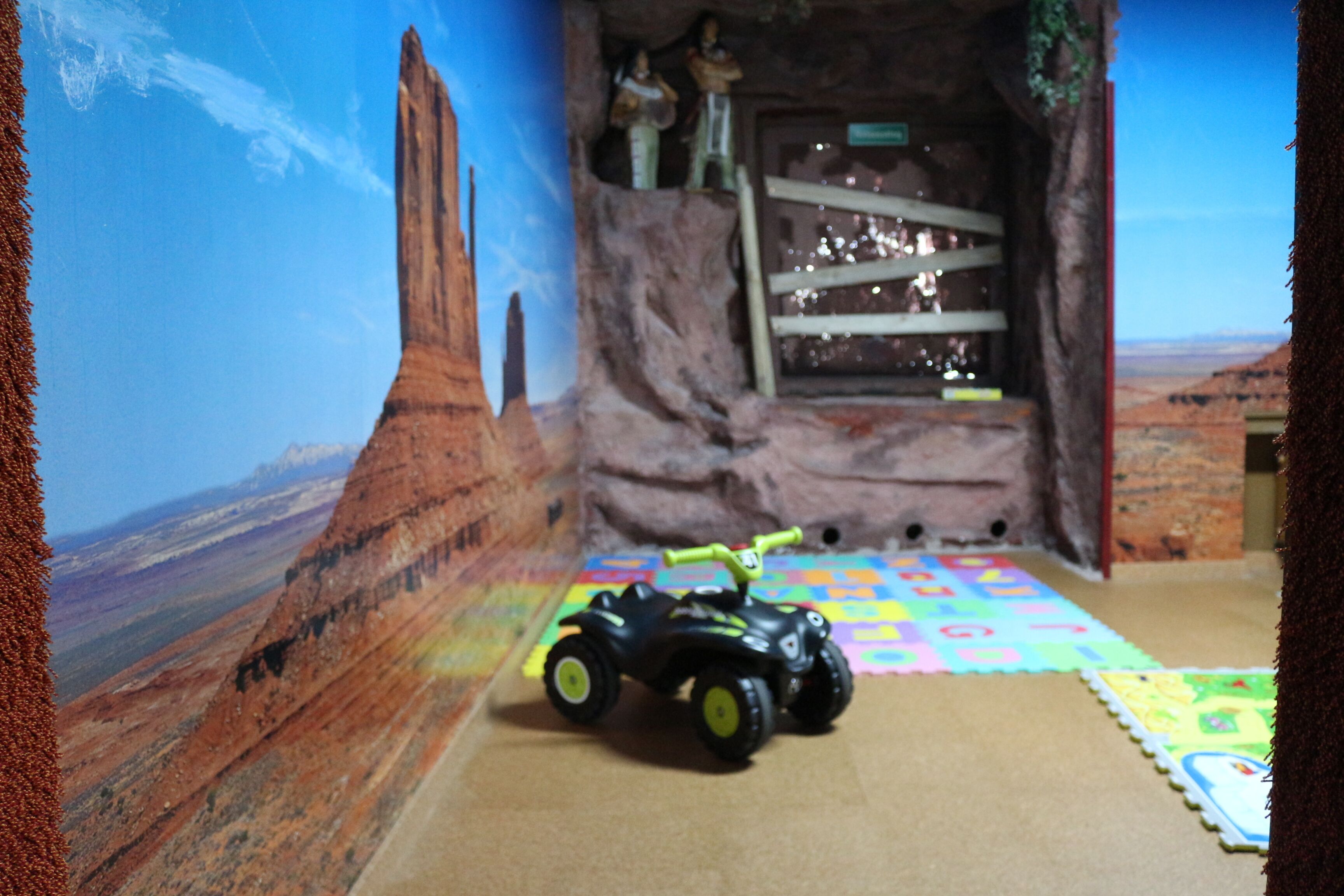 A room with a desert-themed mural, a toy car, and a play mat.