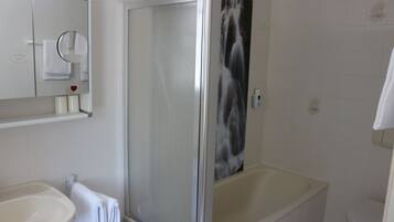 Een badkamer met een douche in een glazen cabine, een bad, een wastafel en een spiegel.