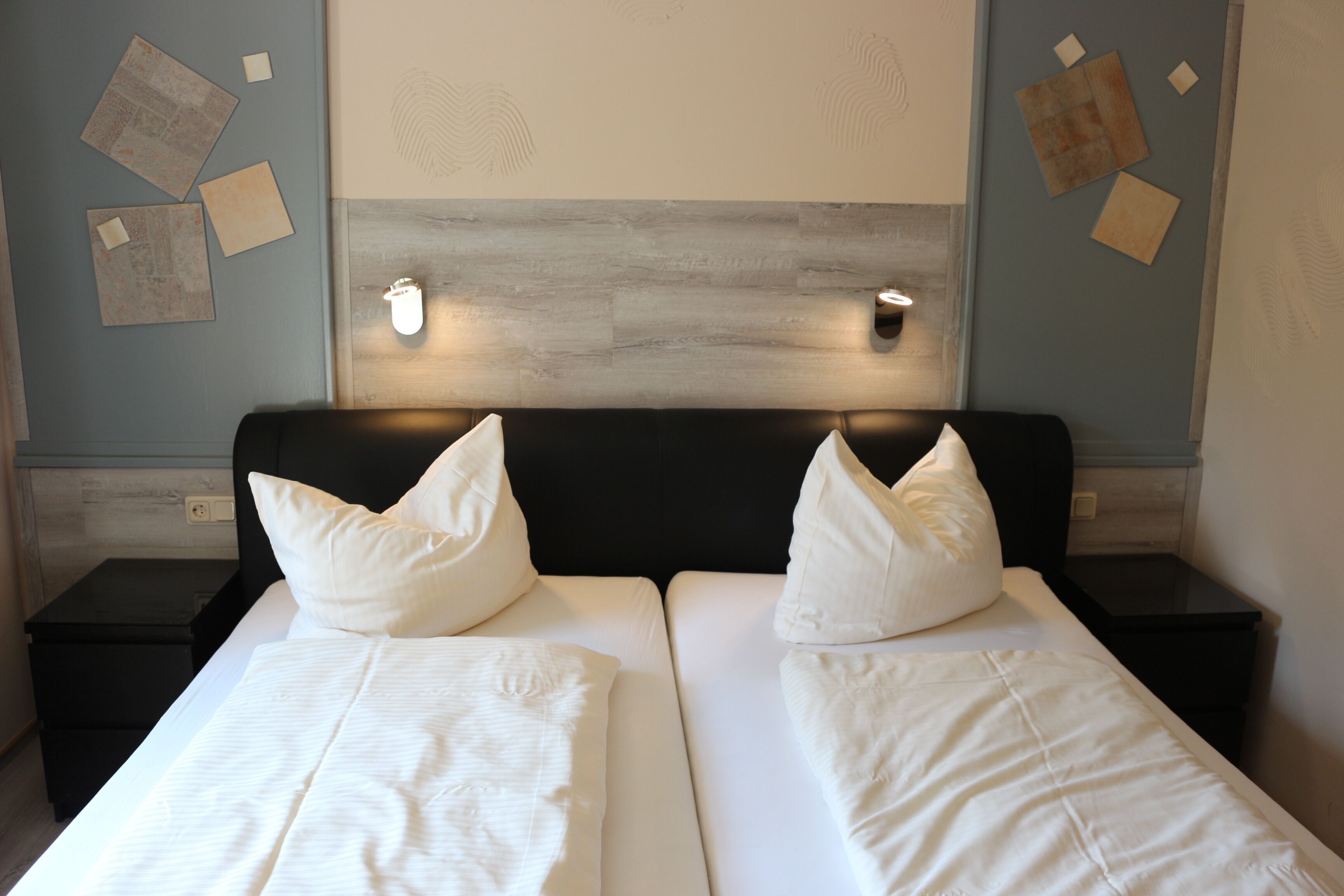 Ein Doppelbett mit weißer Bettwäsche und zwei Kissen, ein Kopfteil mit einer Lampe sowie eine Wand mit angepinnten Papieren.