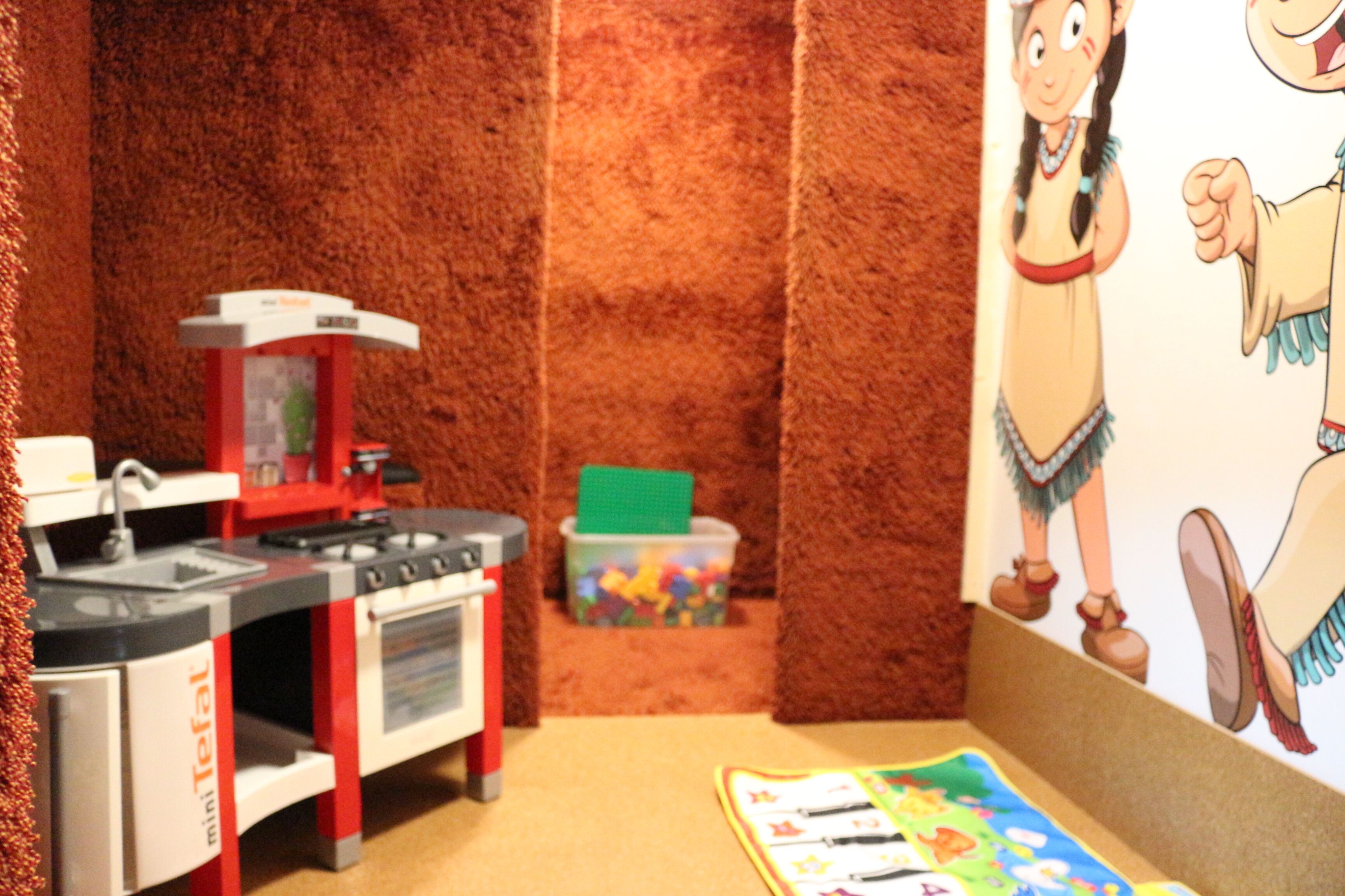 A children's play area with a kitchen playset, a toy chest, and a wall mural.