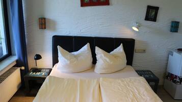 A neatly made bed with white bedding and pillows, a bedside table with a lamp, and a small shelf with books.