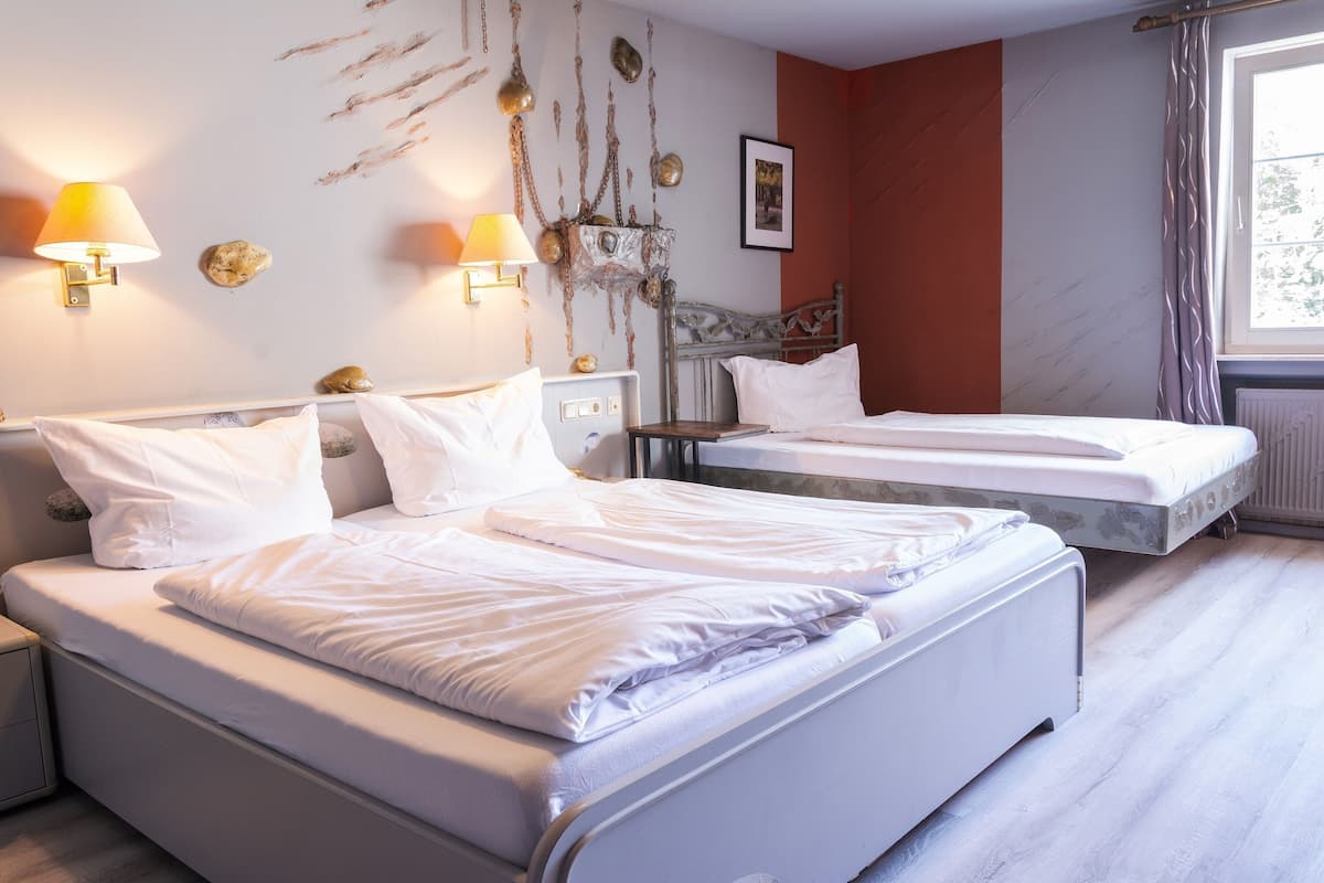 Hotellihuone, jossa on kaksi sänkyä, yöpöytä, lamppu ja ikkuna, jossa on verhot.