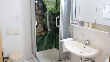 A bathroom with a glass-enclosed shower, a toilet, and a sink.