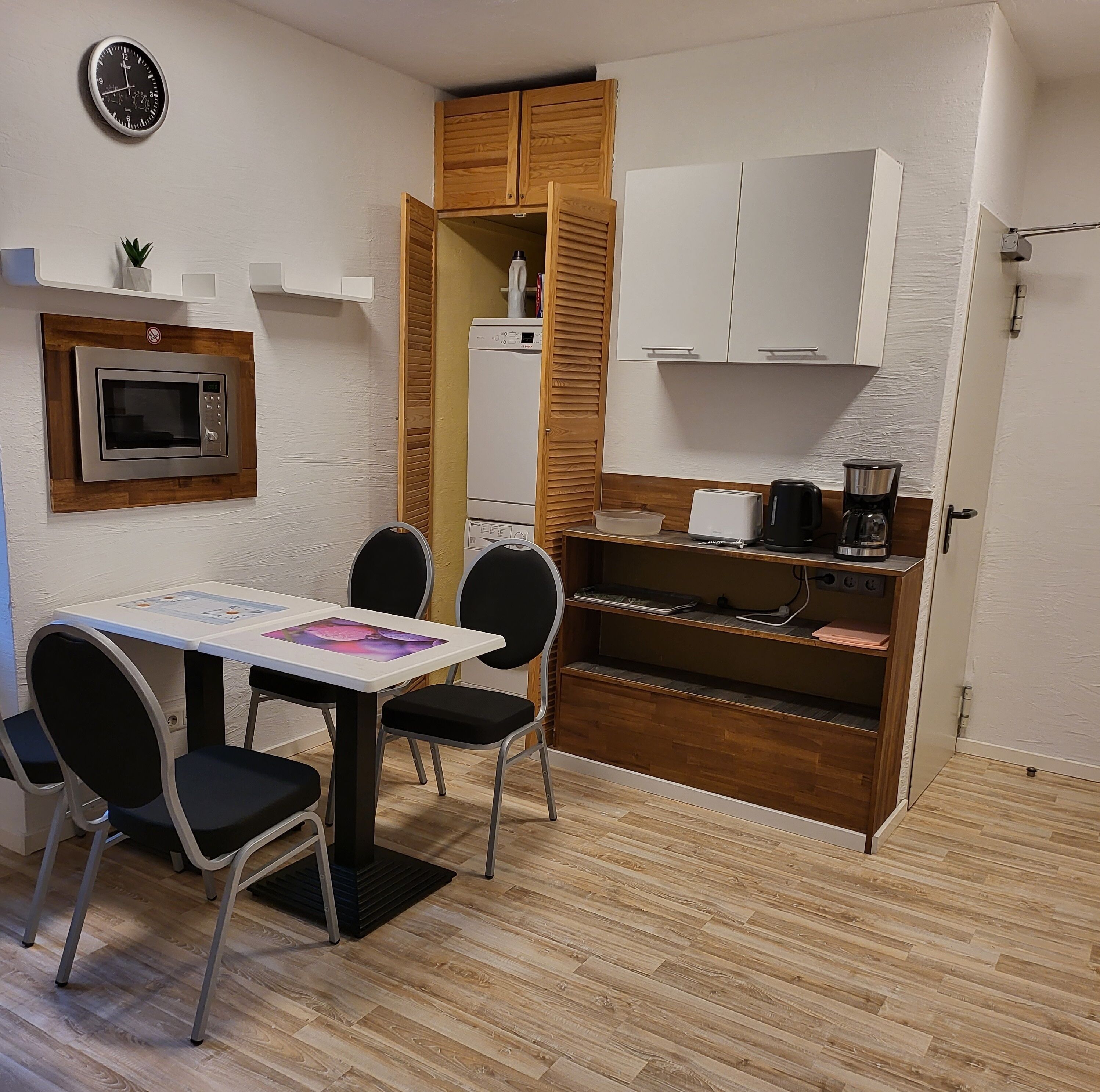 A compact kitchenette with a microwave, toaster, and coffee maker. There is a small dining area with a table and chairs.