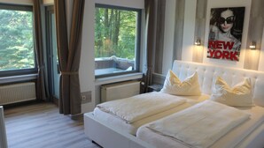 A bedroom with a large bed, a window with a view of trees, and a poster on the wall. - Waldgasthaus am Schwarzenbruch (Allenbach)
