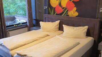 Ein Doppelbett mit weißen Bettwäsche, ein Kopfteil mit floralem Gemälde und ein Fenster mit Vorhängen.