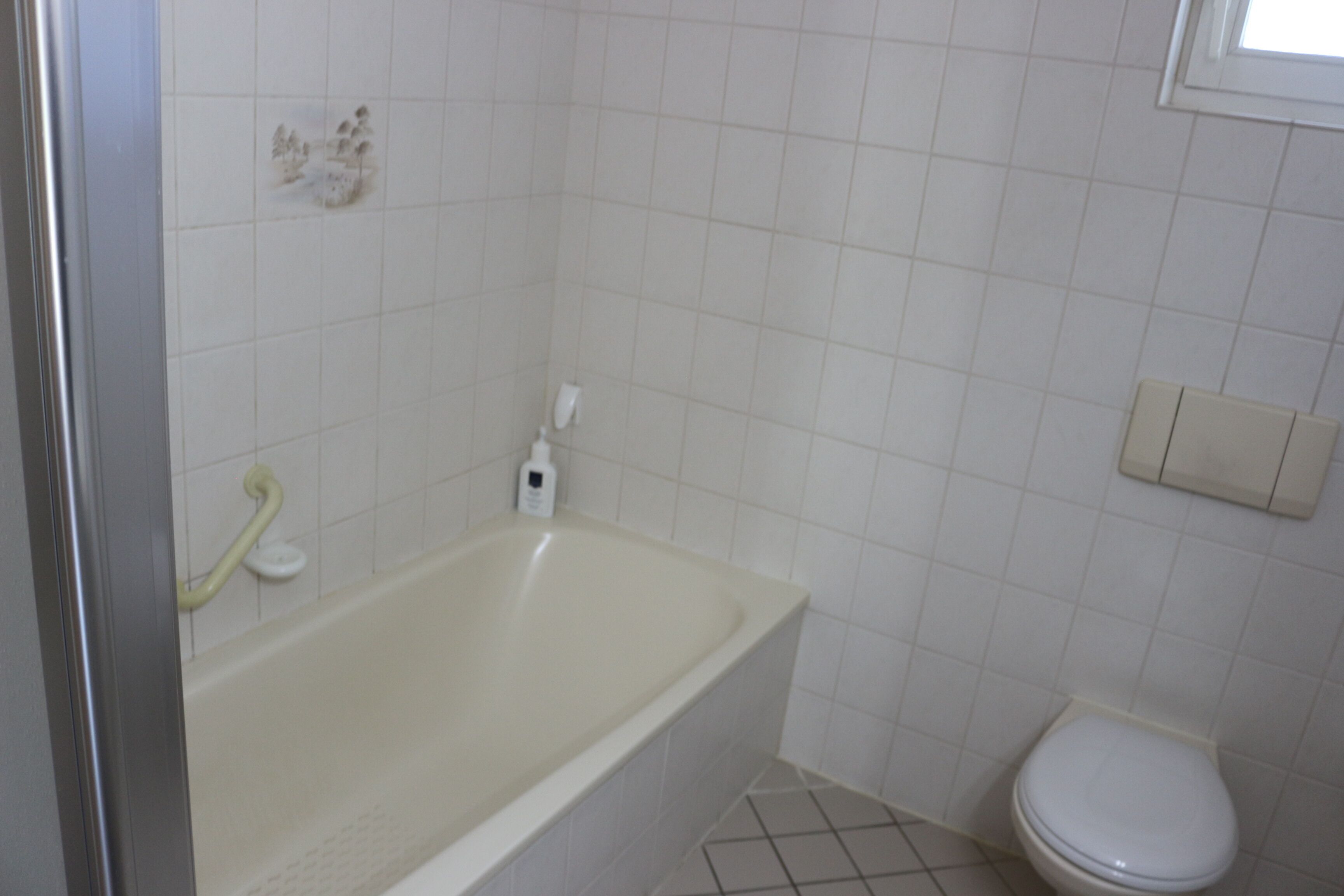 A bathroom with a bathtub, toilet, and a handrail.