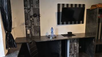 A modern room with a dark wooden desk, a black chair, a flat-screen TV mounted on the wall, and a patterned curtain.