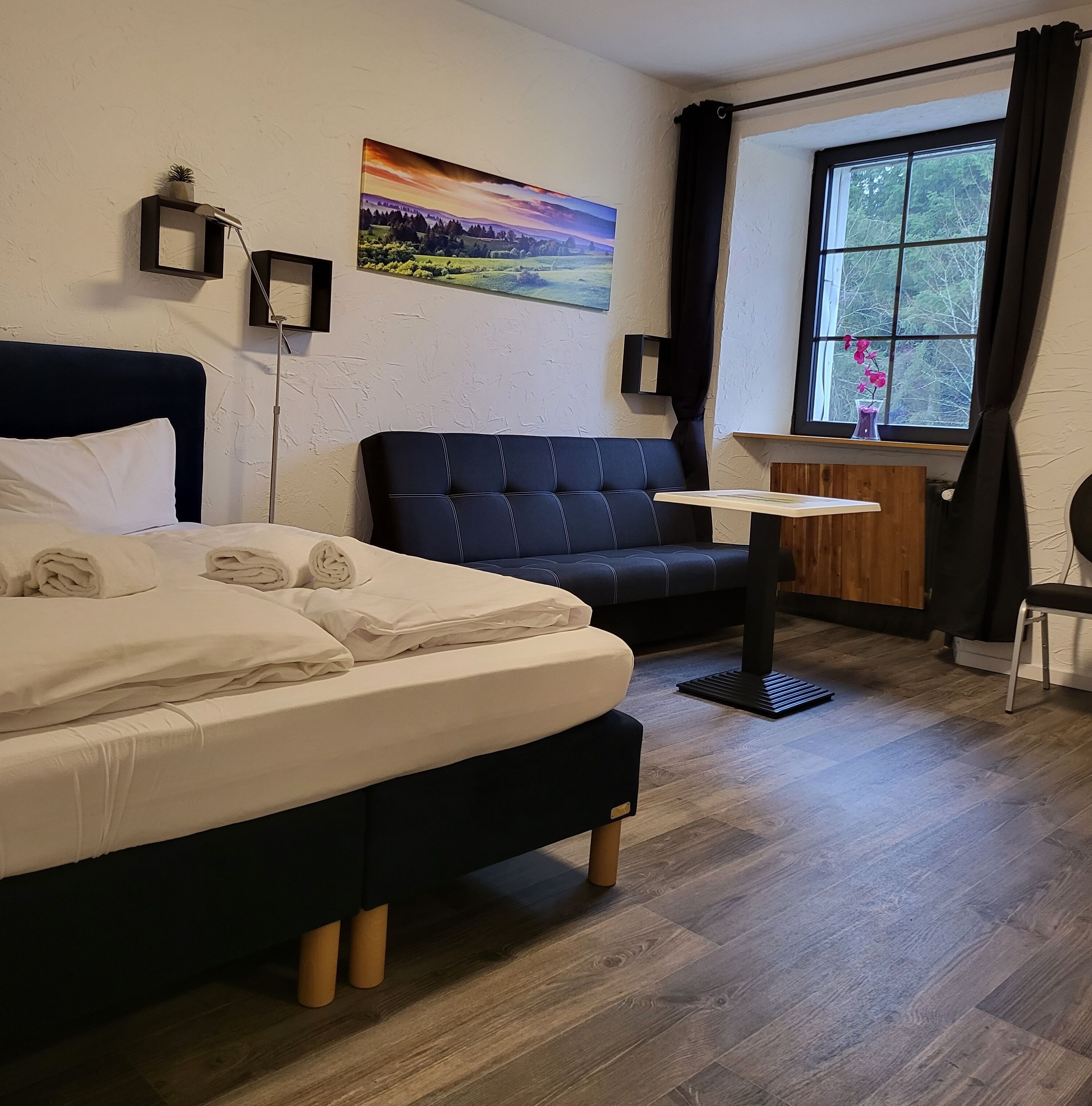 Ein Hotelzimmer mit einem Bett, einem Sofa, einem kleinen Tisch und einem Fenster mit Vorhängen.